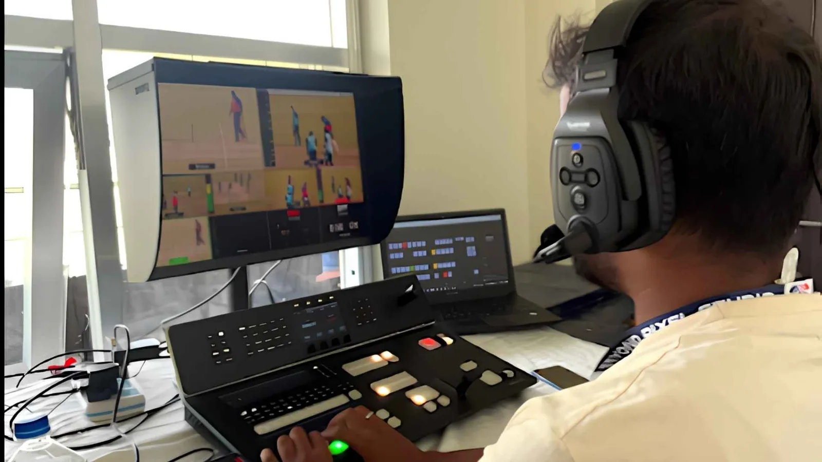 An operator in headphones at the vision switcher, the match live on the monitor in front of him