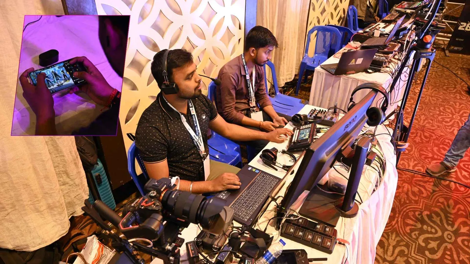 The esports production desk under stage lighting — operators working a long row of monitors and control surfaces