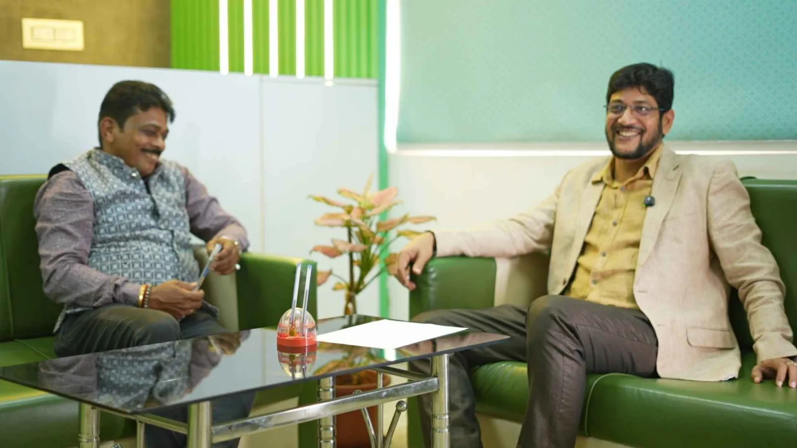 Two guests mid-conversation on the podcast set, seated either side of a low glass table