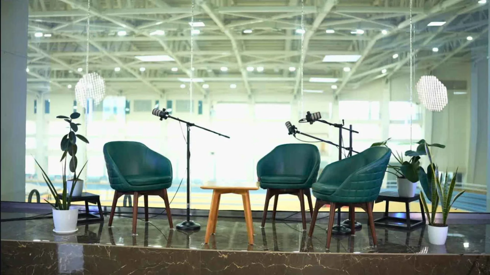 The podcast set lit and rigged before the guests arrive — armchairs, boom microphones and planting against a glazed wall